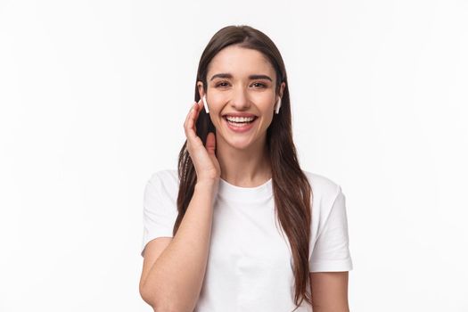 Close-up portrait of attractive smiling happy woman, touching wireless headphone, using earphones to contact friend, having phone conversation with earbuds, laughing carefree.