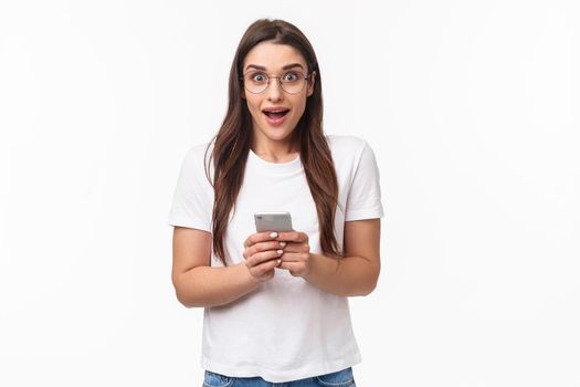 Communication, technology and lifestyle concept. Portrait of impressed, excited pretty girl receive great news, awesome notification from shopping app, gonna buy, hold mobile phone.