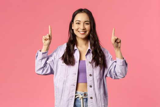 Spring, fashion and people concept. Cheerful young pretty girl in denim jacket, pointing fingers up as showing advertisement, beaming smile camera, inviting to click link, follow or subscribe.
