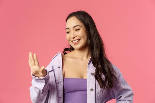 Close-up portrait of pleased good-looking asian girl pleased with great neat manicure, looking at her fingers with smiling satisfied expression, visited nails salon, standing pink background.