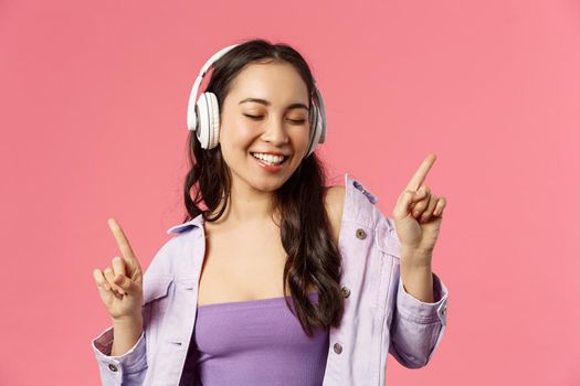 Lifestyle, music and technology concept. Close-up portrait of carefree, happy smiling asian woman enjoying favorite singer new song, dancing with closed eyes, listen songs in headphones.