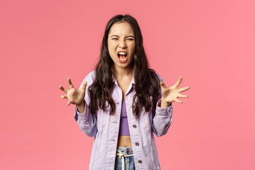 Portrait of aggressive young bothered girl losing temper, screaming furious and angry grimacing, yelling at person with hate and aggression, squeeze hands into fists, pissed-off, pink background.