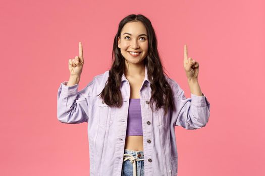 Fashion, beauty and lifestyle concept. Portrait of young stylish woman in denim jacket, crop-top pointing fingers up, smiling and look amused, interested, found product, show promo.