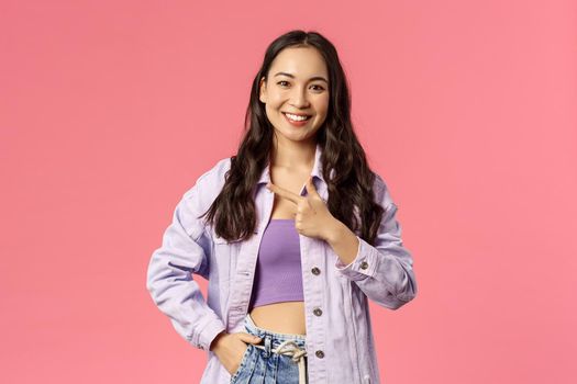 Portrait of charismatic pretty young woman in stylish streetstyle spring outfit, look camera, smiling and pointing left, inviting to event or check out product, advertisement concept.