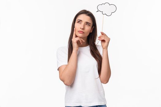 Entertainment, fun and holidays concept. Portrait of thoughtful and creative young woman searching inspiration, holding thinking cloud near head, squinting and look focused up, pondering.