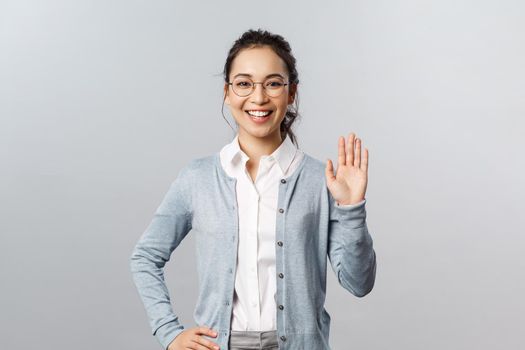 Lifestyle, people and emotions concept. Friendly enthusiastic asian woman in glasses, waving hand in hello, hi gesture, informal greeting of students during online lecture at app, smiling cheerful.
