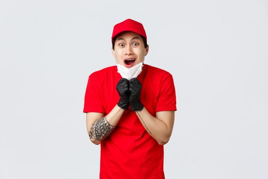 Freak out, shocked asian delivery guy gasping, drop jaw from amazement, take-off medical mask and staring with opened mouth camera. Courier in protective gloves excited looking you.