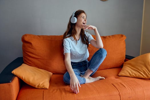 woman listening to music with headphones on the orange sofa Lifestyle. High quality photo