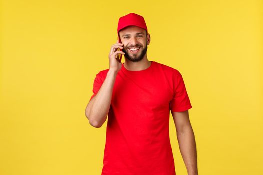 Contactless payment, online delivery, internet shopping and parcel tracking concept. Handsome friendly courier calling customer to pick-up delivery, using mobile phone and smiling camera.