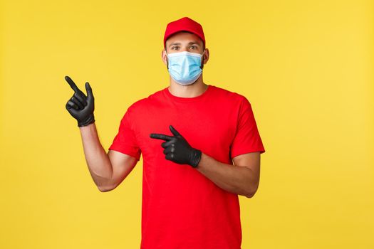 Express delivery during pandemic, covid-19, safe shipping, online shopping concept. Enthusiastic courier in red uniform, medical mask and gloves, pointing fingers left, inform about promo.