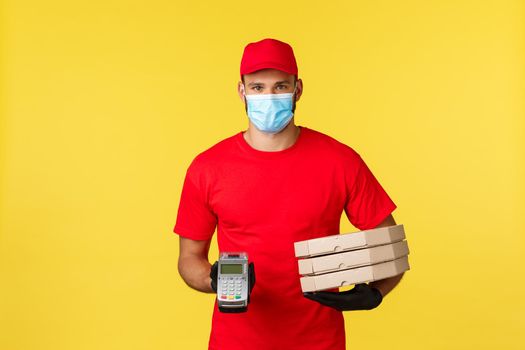 Food delivery, tracking orders, covid-19 and self-quarantine concept. Courier in red uniform cap and t-shirt, medical mask, giving client POS terminal and pizza order.
