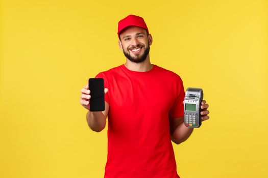 Contactless payment, online delivery, internet shopping concept. Nice courier in red uniform t-shirt and cap, showing customer smartphone app and paying terminal POS, yellow background.