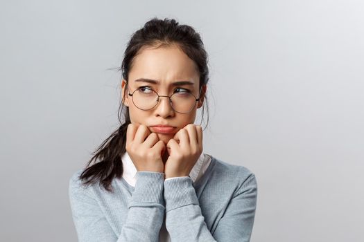 Close-up of gloomy offended young silly asian woman, sulking frowning upset, look left with envy or regret, have hard feelings, insulted of unfair situation happened her, stand grey background.