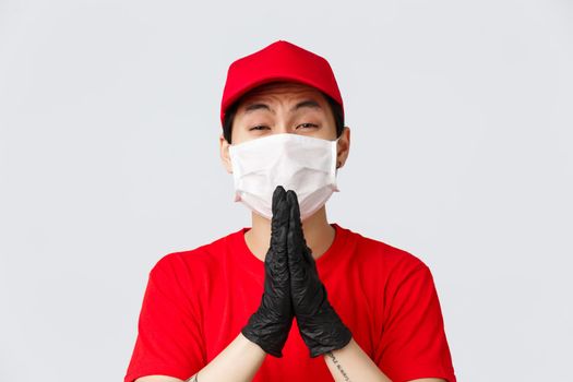 Covid-19, self-quarantine online shopping and delivery concept. Clingy asian courier in medical mask and gloves, begging for favour, pleading for favour, need help, standing grey background.