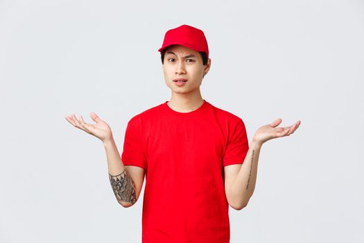 Express delivery, shipping and logistics concept. Courier dont understand why, wearing red cap and t-shirt, shrugging with hands spread sideways, grimacing bothered, complain.