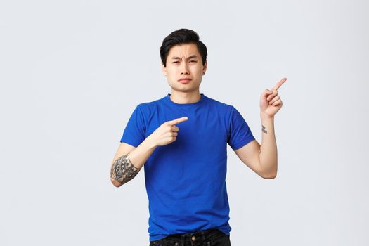 Different emotions, people lifestyle and advertising concept. Displeased and sad asian man in blue t-shirt, pointing fingers right, sobbing and whining, complaining jealous and bothering situation.