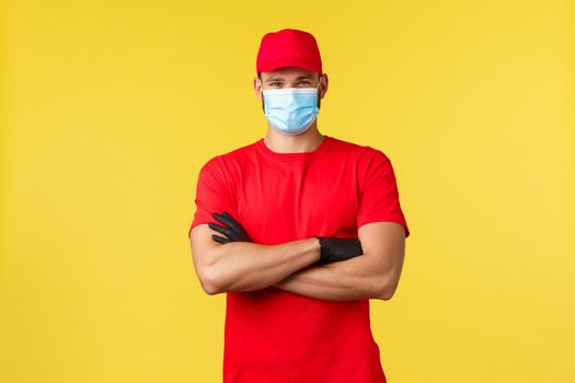 Express delivery during pandemic, covid-19, safe shipping, online shopping concept. Confident serious courier in red uniform, cross arms determined, wear medical mask, deliver orders to clients.
