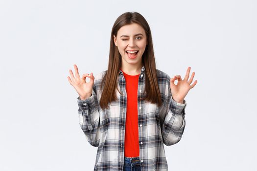 Lifestyle, different emotions, leisure activities concept. Confident and assured enthusiastic young woman in checked shirt assure all okay, promise or guarantee, show okay sign, smiling and wink.