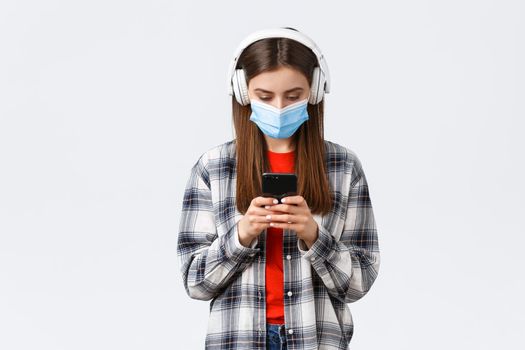 Social distancing, leisure and lifestyle on covid-19 outbreak, coronavirus concept. Cute female student, teenage girl in headphones picking song in mobile phone, download music app, white background.