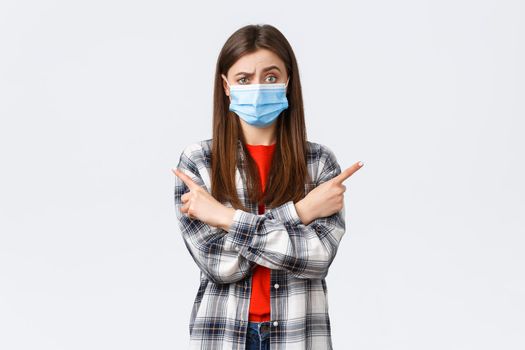 Coronavirus outbreak, leisure on quarantine, social distancing and emotions concept. Indecisive and clueless pretty girl in medical mask ask your opinion, advice as pointing sideways left and right.