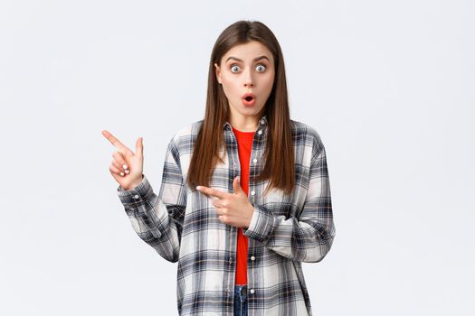 Lifestyle, different emotions, leisure activities concept. Impressed female customer, girl in casual checked shirt, say wow talking about news and pointing fingers left, white background.