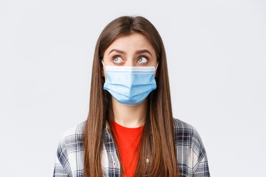 Coronavirus outbreak, leisure on quarantine, social distancing and emotions concept. Close-up of thoughtful, young woman in medical mask, look upper left corner reading sign or have bubble thought.