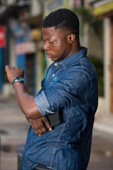 young man with serious face watches watch in hand waiting for a late meeting in the street in the evening
