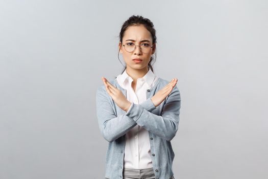 We must end it. Serious-looking determined young confident asian woman, making cross stop sign and looking concerned camera, prohibit something, disagree, trying restrict from going outside.