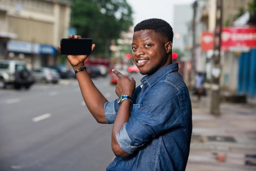smiling young man in casual outfit presenting new product on a cell phone in the street