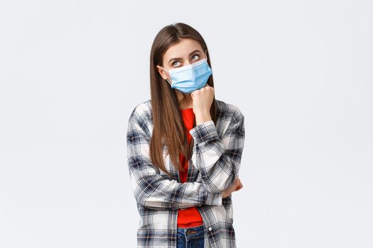 Coronavirus outbreak, leisure on quarantine, social distancing and emotions concept. Thoughtful and gloomy young woman hate staying home self-isolation, dreaming go vacation, wear medical mask.
