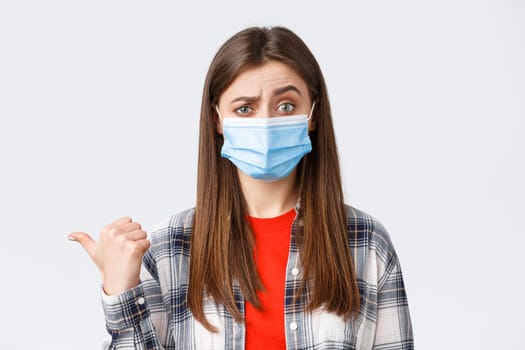 Coronavirus outbreak, leisure on quarantine, social distancing and emotions concept. Skeptical young woman in medical mask express disbelief towards banner to the left, pointing doubtful.