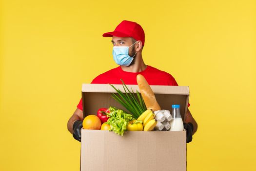 Takeaway delivery, covid-19 quarantine and groceries concept. Enthusiastic courier in red uniform, medical mask, look cheeky, bring customer food deliver, online order to doorstep.