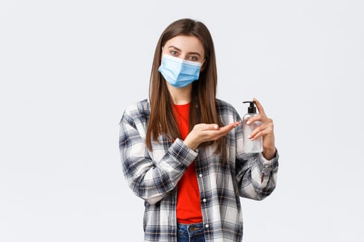 Coronavirus outbreak, leisure on quarantine, social distancing and emotions concept. Friendly smiling girl in medical mask using hand sanitizer to keep safe during covid-19 pandemic.