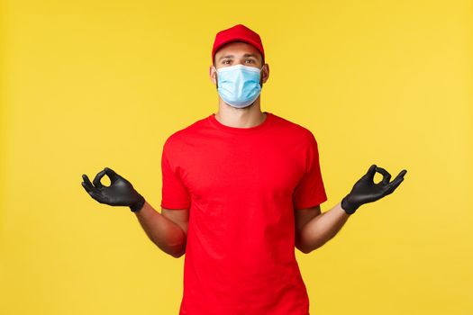 Express delivery during pandemic, covid-19, safe shipping, online shopping concept. Calm and peaceful courier in red uniform, medical mask and gloves, hold hands zen, meditating, yellow background.