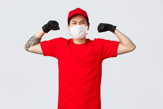 Strong asian delivery guy in red cap, t-shirt show-off his strength, flex biceps bragging muscles as carry large boxes at work. Courier easily deliver heavy parcels. Concept of carriers and shopping.