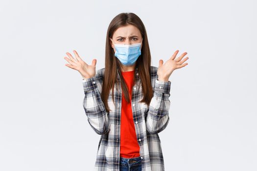 Different emotions, covid-19 pandemic, coronavirus self-quarantine and social distancing concept. Angry, outraged woman in medical mask, arguing, look mad, raise hands in dismay, complaining.