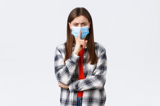 Coronavirus outbreak, leisure on quarantine, social distancing and emotions concept. Serious-looking girl in medical mask, shushing with irritated face, frowning tell be quiet or keep silence.