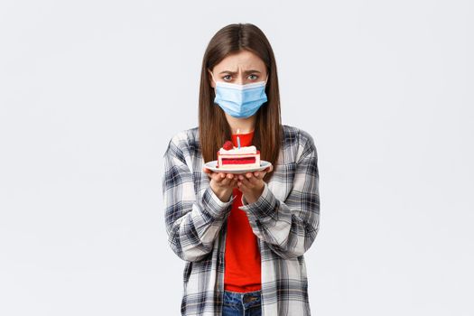 Coronavirus outbreak, lifestyle on social distancing and holidays celebration concept. Lonely and upset cute girl in medical mask, celebrating birthday all alone on self-quarantine, sob and hold cake.