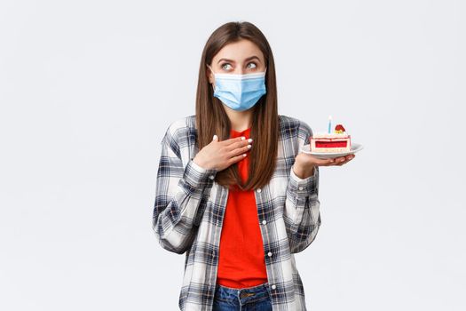 Coronavirus outbreak, lifestyle during social distancing and holidays celebration concept. Dreamy attractive woman in medical mask making wish as holding birthday cake, look away imaging.