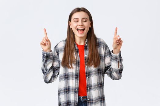 Lifestyle, different emotions, leisure activities concept. Dreamy and happy pretty young woman in checked shirt, dream came true, showing summer vacation resort, pointing fingers up with closed eyes.