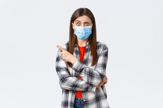 Coronavirus outbreak, leisure on quarantine, social distancing and emotions concept. Confused and worried girl asking question about smth strange, pointing finger left, wear medical mask covid-19.