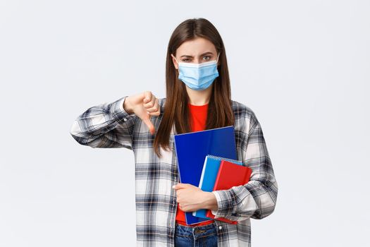 Coronavirus pandemic, covid-19 education, and back to school concept. Displeased and disappointed female student, freshman in medical mask thumb-down and grimacing discussing smth bad.