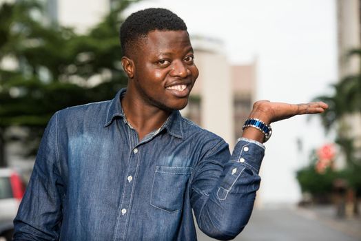 portrait of young happy man in shirt gesturing a welcome sign showing something of the hand