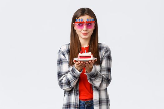 People lifestyle, holidays and celebration, emotions concept. Cute and silly birthday girl in funny glasses, look away think of wish as blowing lit candle on b-day cake, smiling excited.