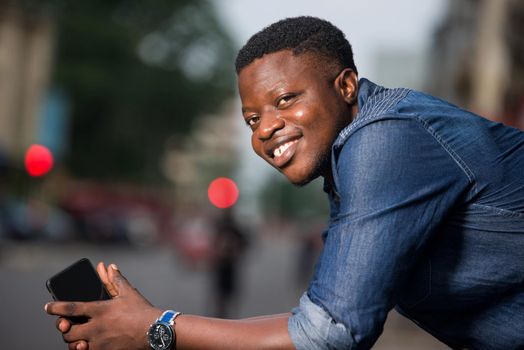 young african man with mobile phone looking at camera smiling.