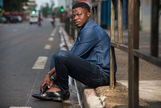 young man sitting in jeans looking at camera with frowning eyebrows.