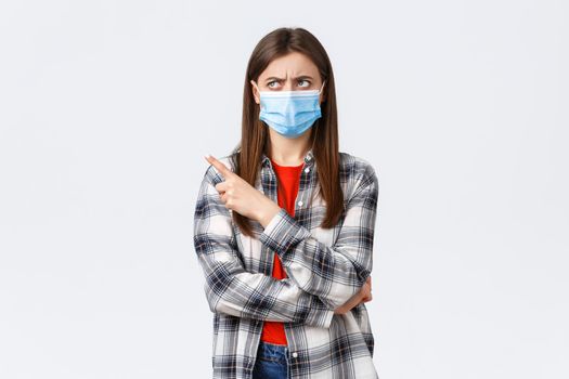 Coronavirus outbreak, leisure on quarantine, social distancing and emotions concept. Skeptical young girl express disbelief, frowning, looking and pointing upper left corner, wear medical mask.