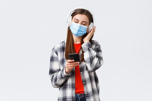 Social distancing, leisure and lifestyle on covid-19 outbreak, coronavirus concept. Carefree and relaxed woman in medical mask, close eyes enjoying music in headphones, hold mobile phone.