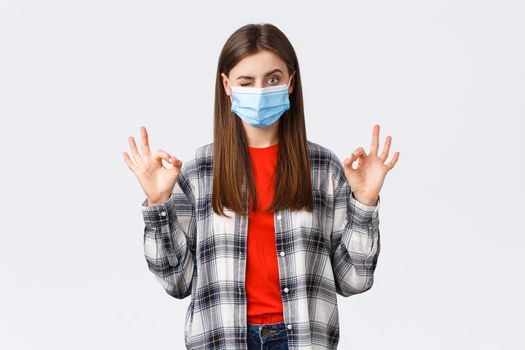 Coronavirus outbreak, leisure on quarantine, social distancing and emotions concept. Determined young woman in medical mask assure all good, show okay signs and wink, no problem.