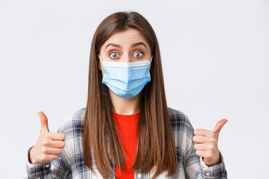 Coronavirus outbreak, leisure on quarantine, social distancing and emotions concept. Sounds good. Excited and pleased, satisfied female in medical mask, show thumb-up, interesting idea.